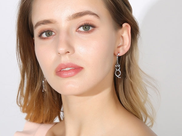 Cat and fishbone rhinestone drop earrings worn by model.