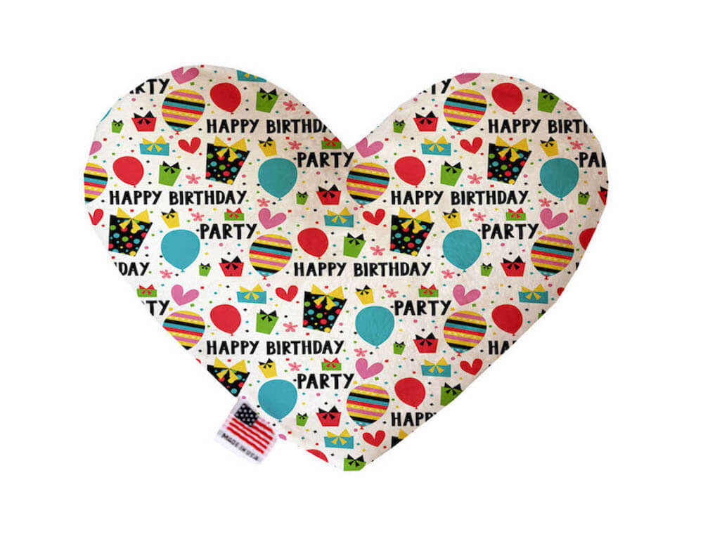 Heart shaped squeaker dog toy. White background with a multicolored "Happy Birthday," balloon, present and heart pattern. Made in USA label on bottom trim.