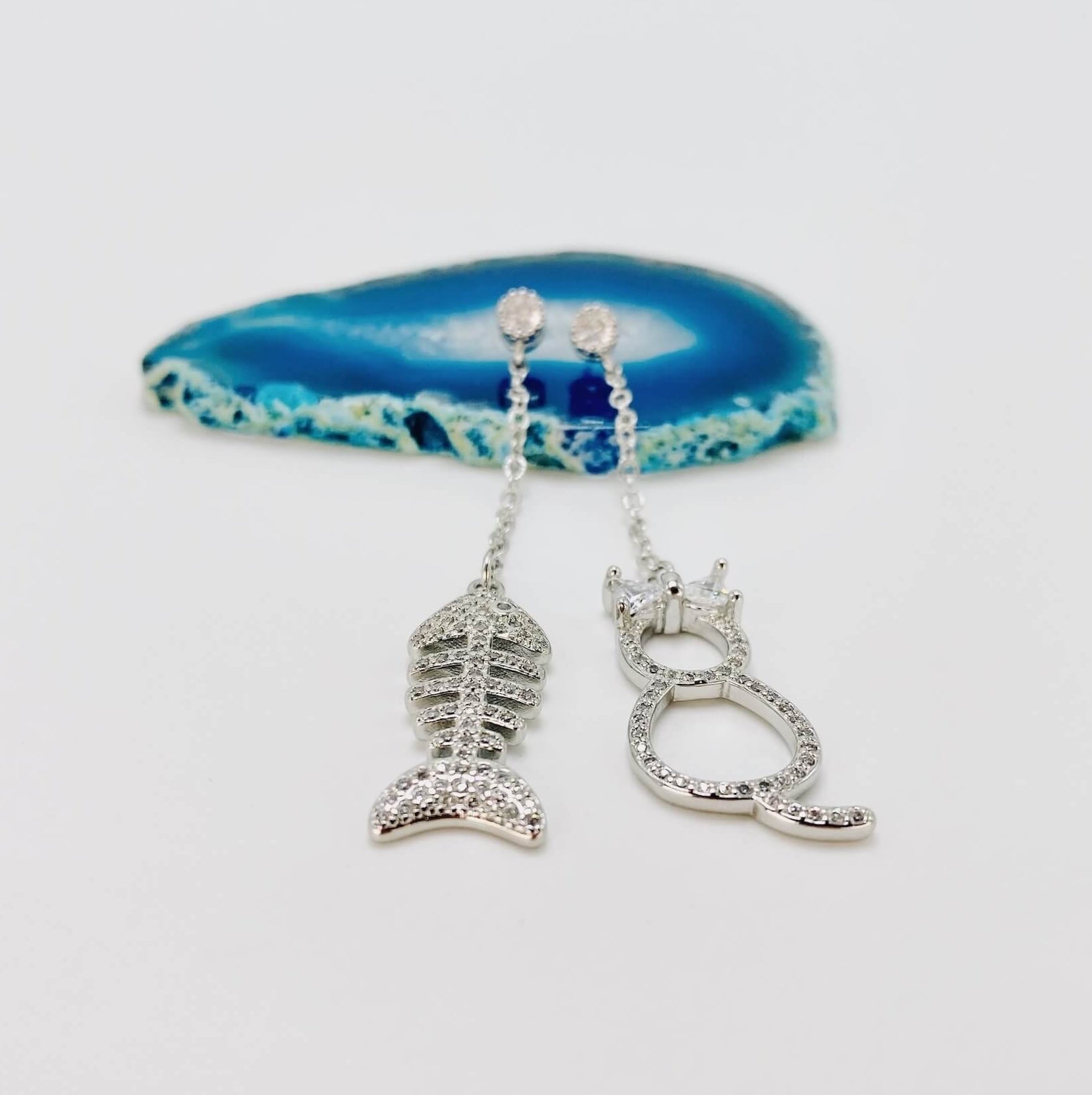 Cat and fishbone rhinestone drop earrings resting on blue agate stone.