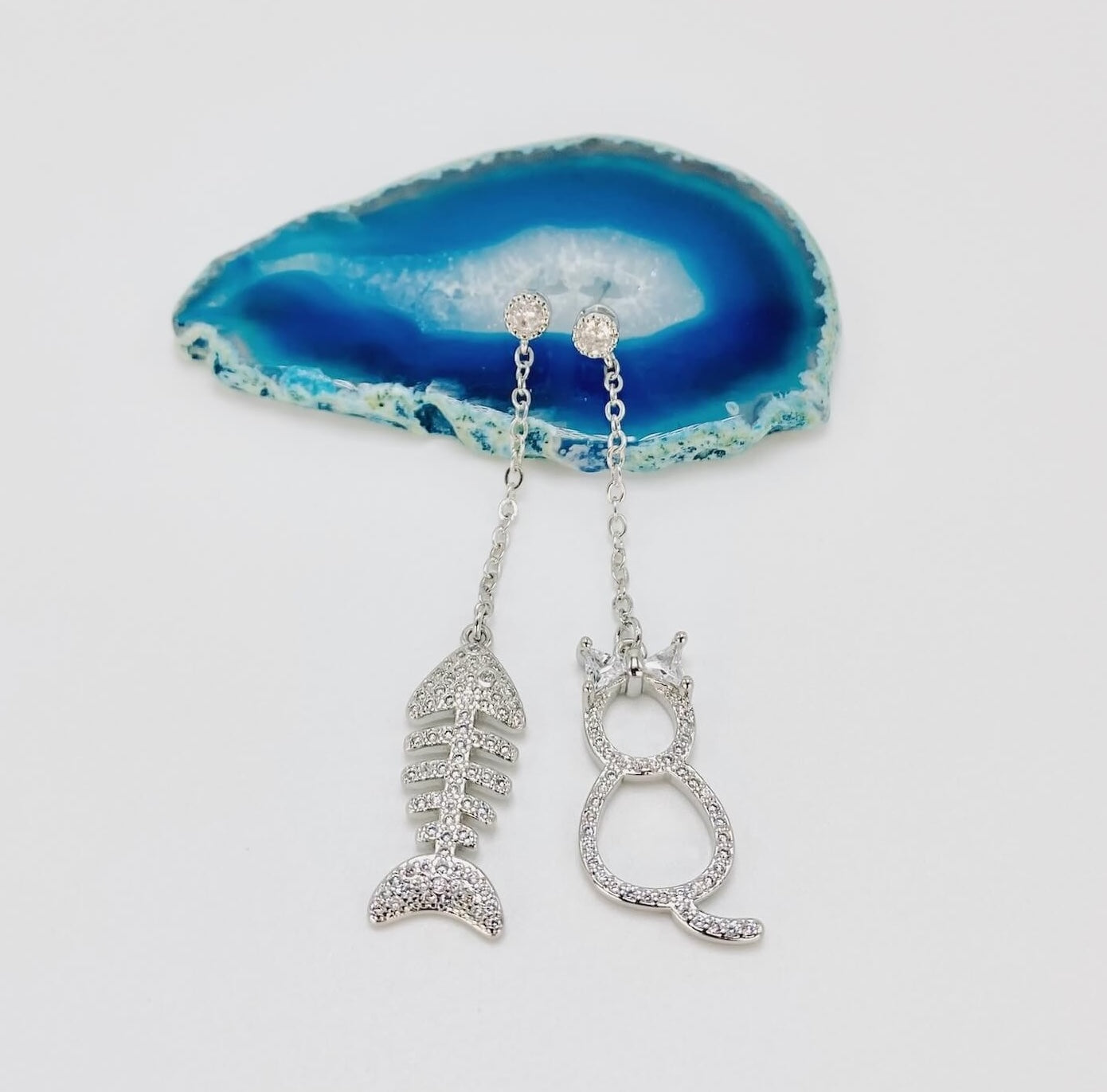 Cat and fishbone rhinestone drop earrings resting on blue agate stone.