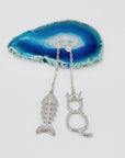 Cat and fishbone rhinestone drop earrings resting on blue agate stone.