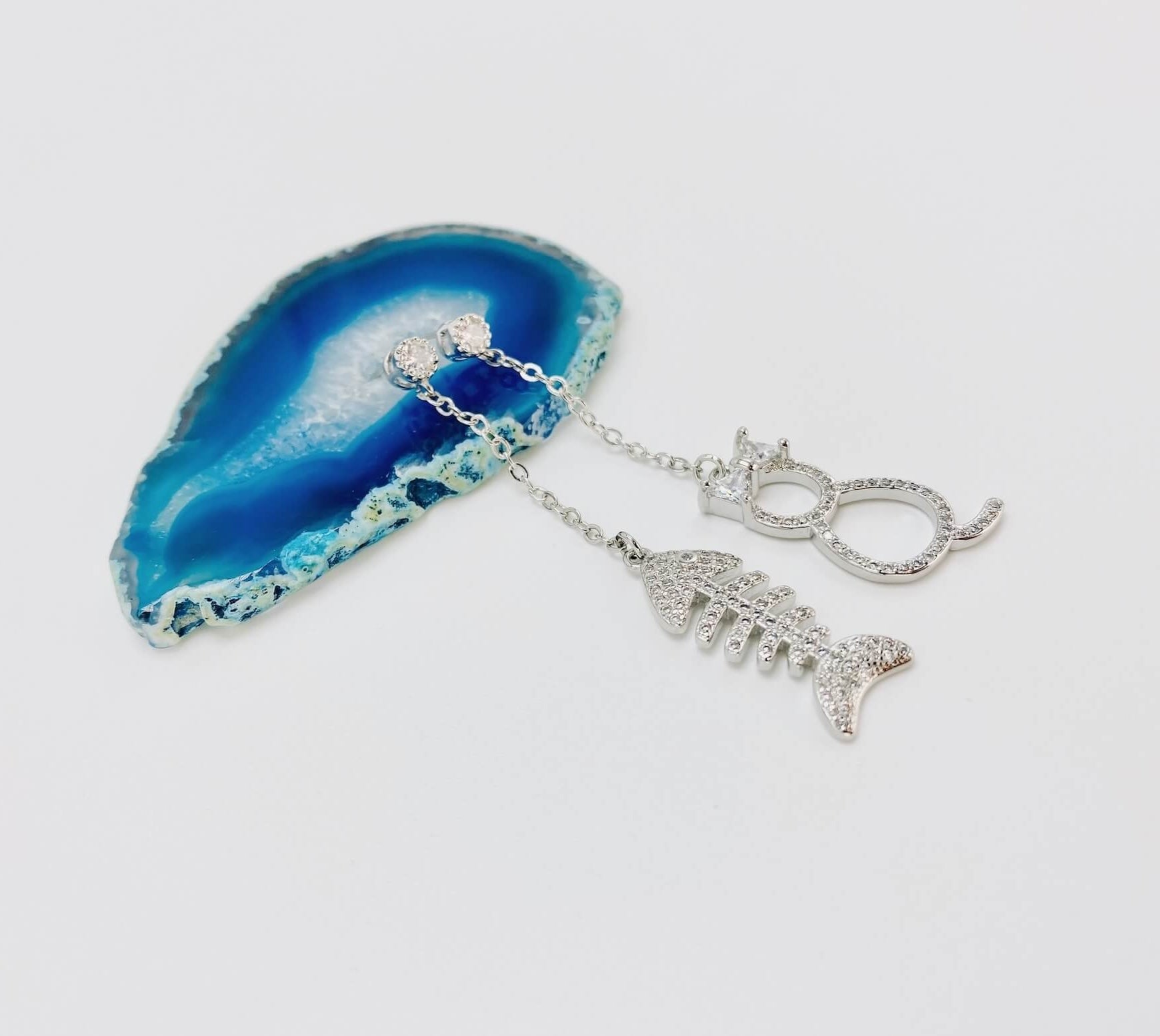 Cat and fishbone rhinestone drop earrings resting on blue agate stone.