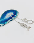 Cat and fishbone rhinestone drop earrings resting on blue agate stone.