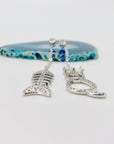 Cat and fishbone rhinestone drop earrings resting on blue agate stone.
