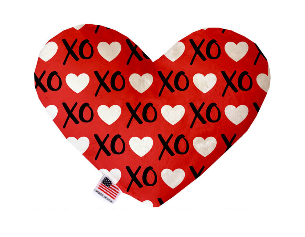 Heart shaped squeaker dog toy. Red background with white hearts and black "XO" text printed throughout. Made in USA label on bottom trim.