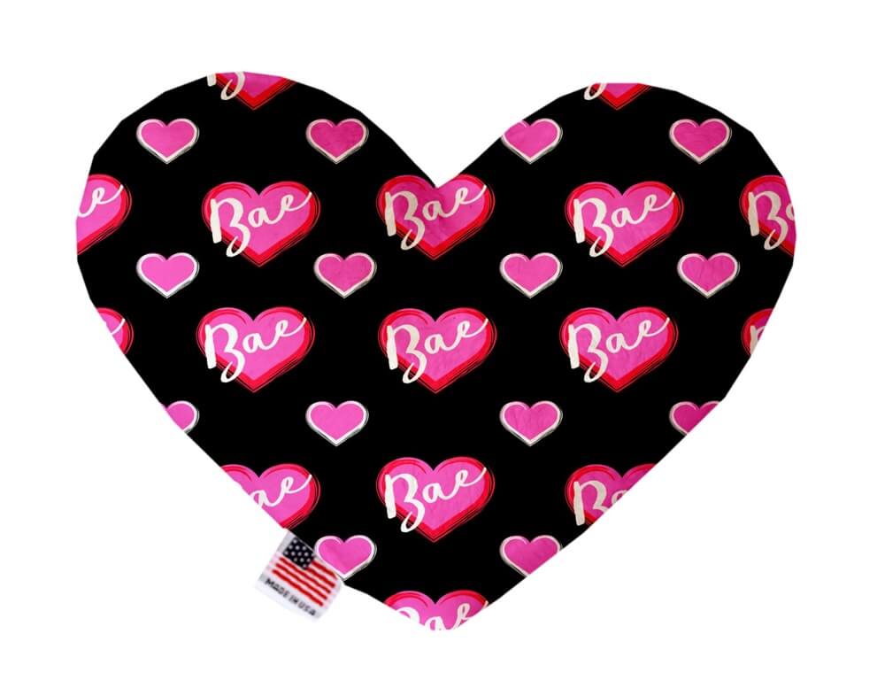 Heart shaped squeaker dog toy. Black background with pink hearts and "Bae" font printed throughout. Made in USA label on bottom trim.