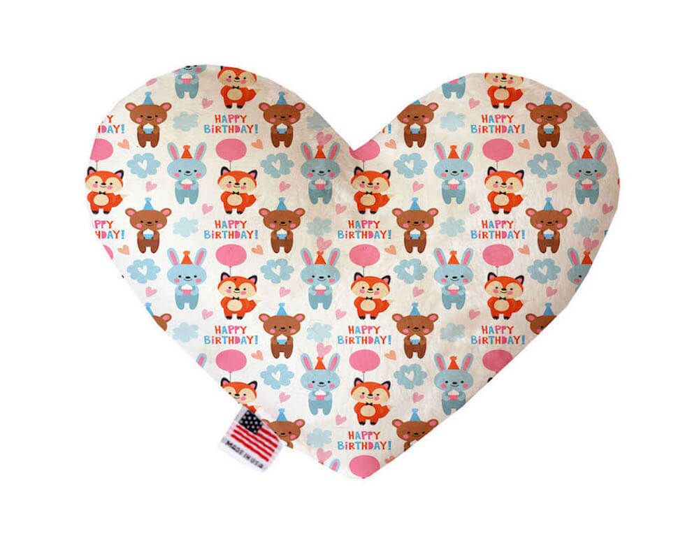 Heart shaped squeaker dog toy. White background with a multicolored print featuring the phrase, "Happy Birthday," as well as bunnies, bears and foxes holding pink balloons. Made in USA label on bottom trim.
