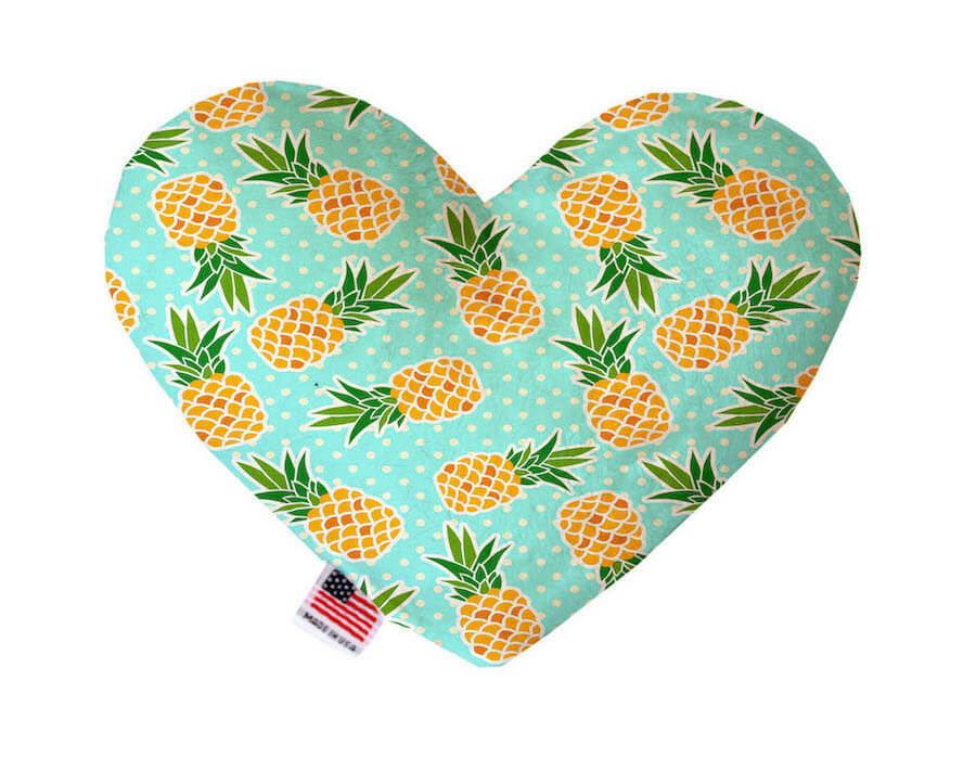 Heart shaped squeaker dog toy. Blue background with yellow pineapples and a white polka dot print. Made in USA label on bottom trim.