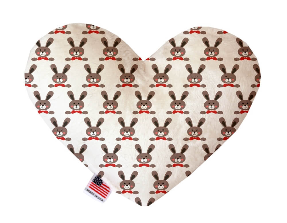 Heart shaped squeaker dog toy. White background with brown bunny faces wearing red bow ties printed throughout. Made in USA label on bottom trim.