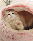 Cat reaching out its paw toward the camera in a pink plush nesting cave bed (short plush version).