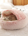 Cat lying down in a pink plush nesting cave bed.