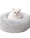 White cat sitting in gray donut plush bed.