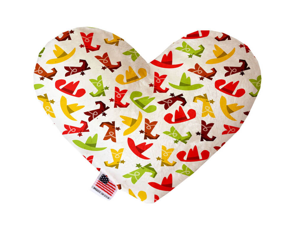 Heart shaped squeaker dog toy. White background with red, yellow, green and brown cowboy hats and boots printed throughout. Made in USA label on bottom trim.