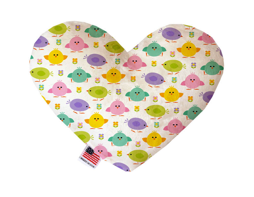Heart shaped squeaker dog toy. White background with purple, yellow, pink and green chicks and flowers printed throughout. Made in USA label on bottom trim.