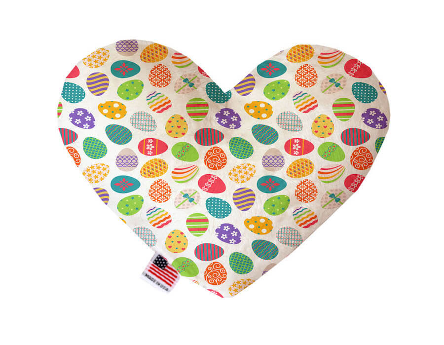 Heart shaped squeaker dog toy. White background with multicolored Easter eggs that have different patterns on them printed throughout. Made in USA label on bottom trim.
