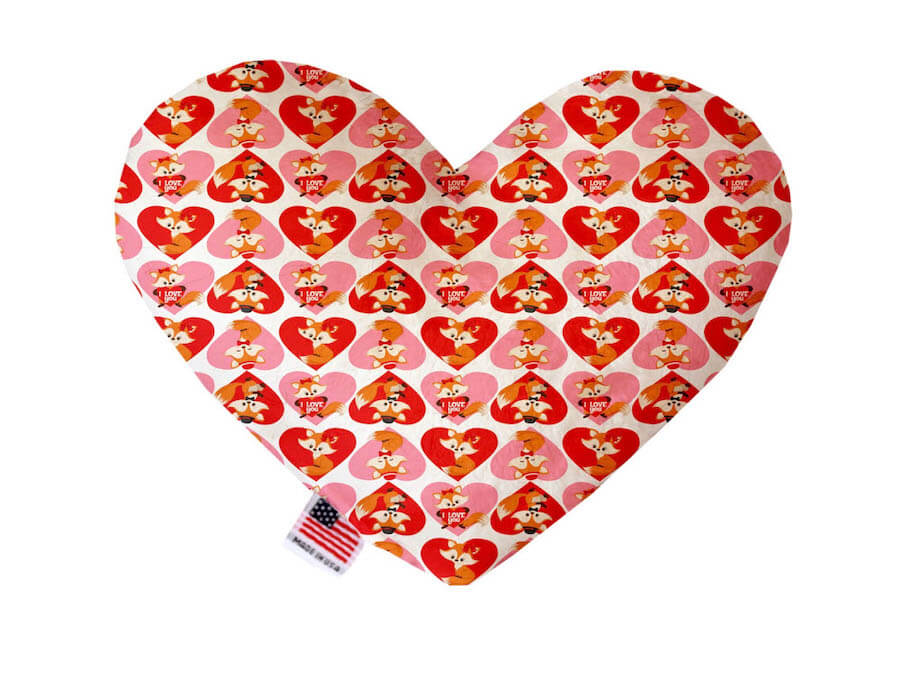 Heart shaped squeaker dog toy. White background with red and pink hearts and orange foxes printed throughout. Made in USA label on bottom trim.