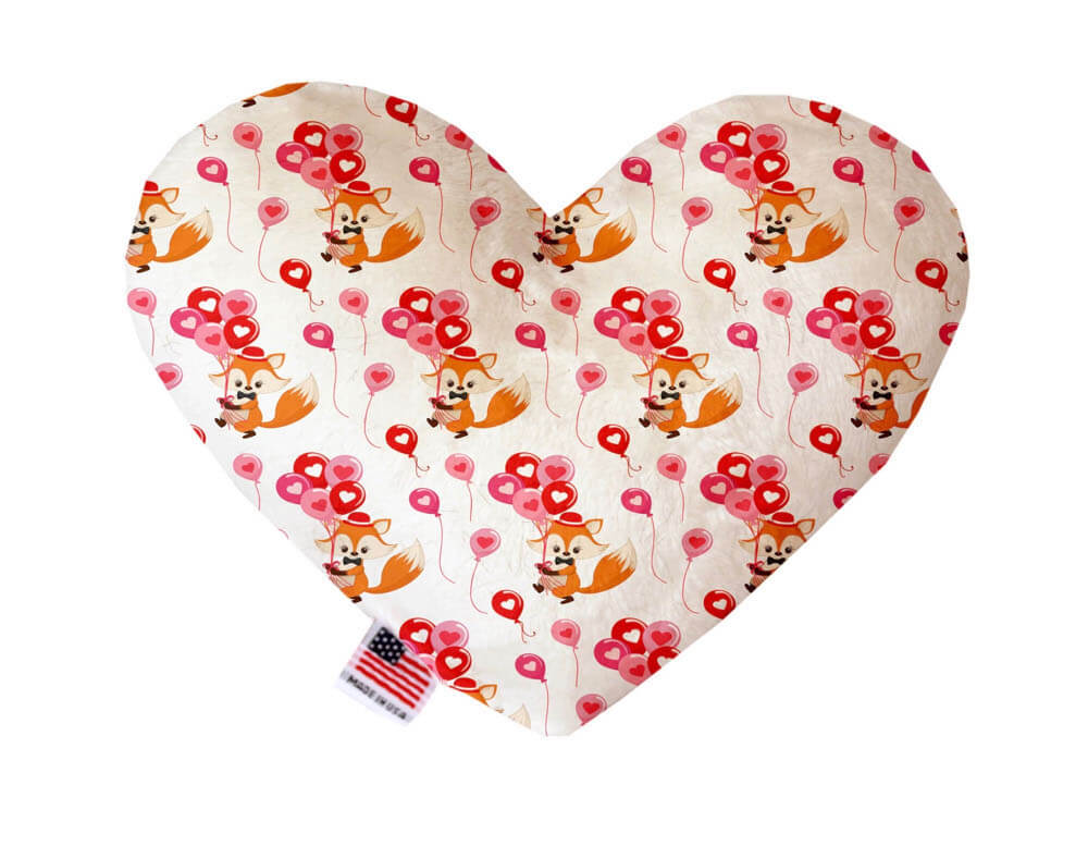 Heart shaped squeaker dog toy. White background with orange foxes carrying red and pink balloons printed throughout. Made in USA label on bottom trim.