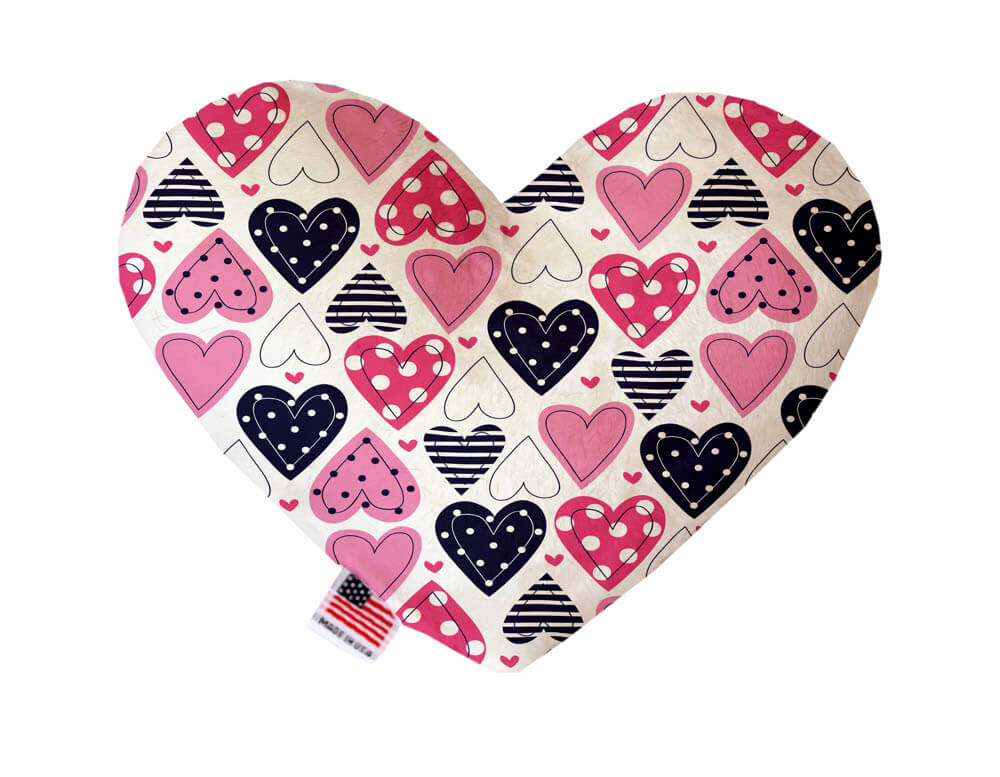 Heart shaped squeaker dog toy. White background with red, pink and blue hearts printed throughout. Made in USA label on bottom trim.