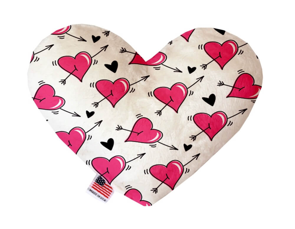 Heart shaped squeaker dog toy. White background with pink hearts and black arrows printed throughout. Made in USA label on bottom trim.
