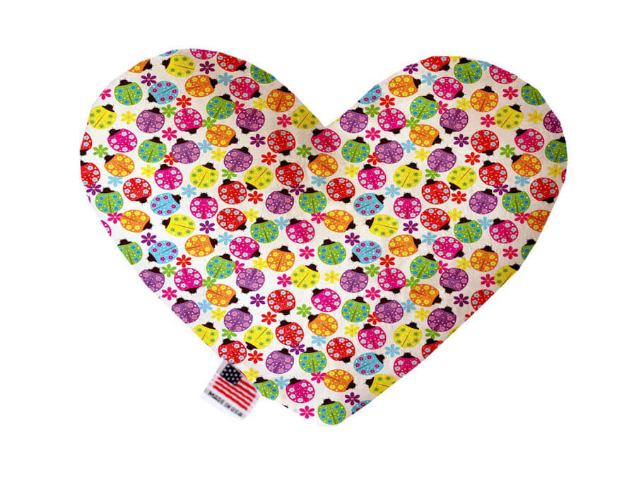 Heart shaped squeaker dog toy. White background with multicolored ladybugs and flowers printed throughout. Made in USA label on bottom trim.