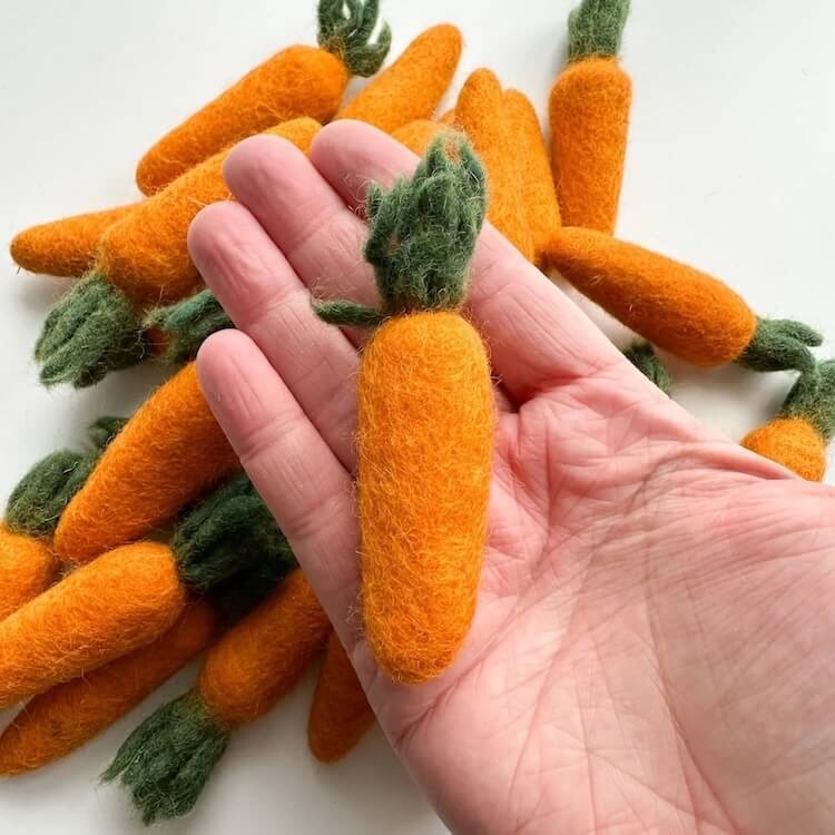 Someone holding an orange carrot felted wool cat toy in their hand to show size and scale.