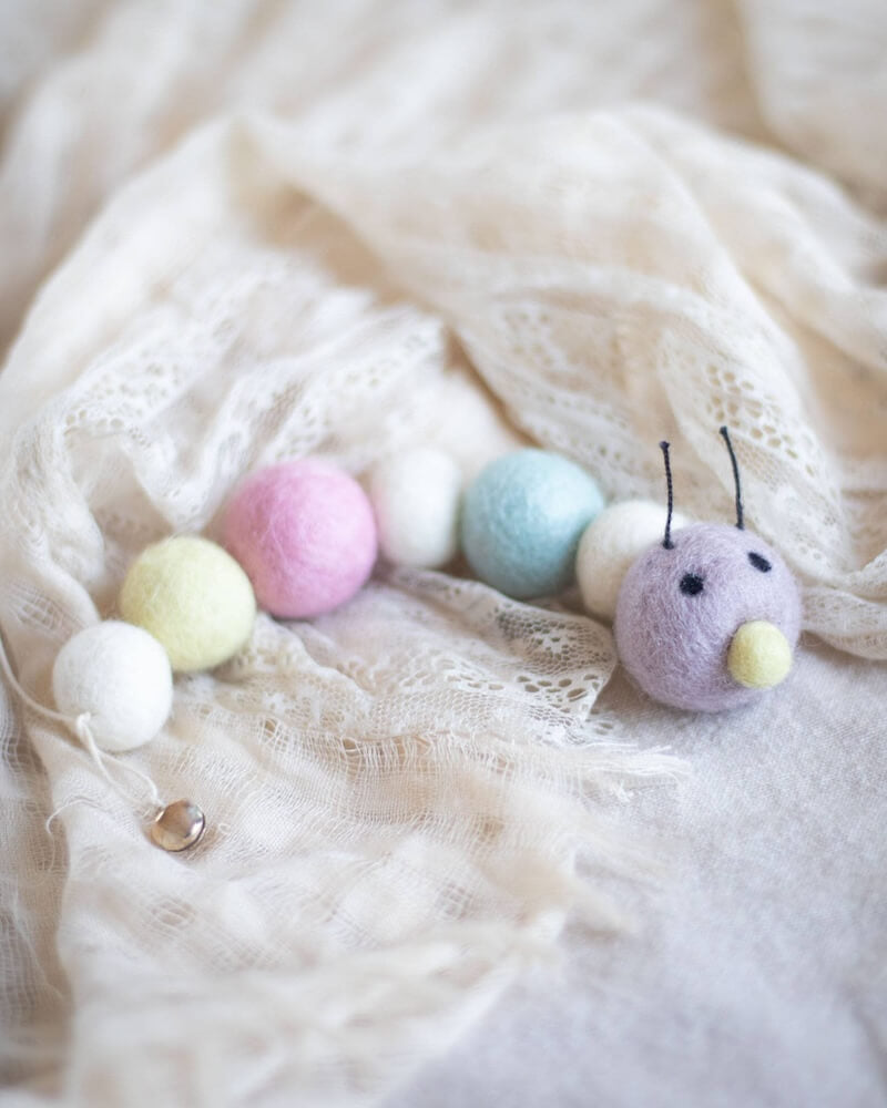 Pastel wool caterpillar cat toy with bell at the end of its tail.