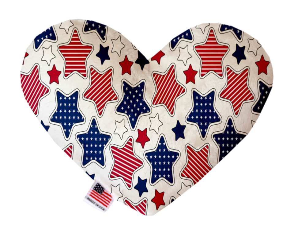 Heart shaped squeaker dog toy. White background with red and blue stars printed throughout. Patriotic, 4th of July themed. Made in USA label on bottom trim.