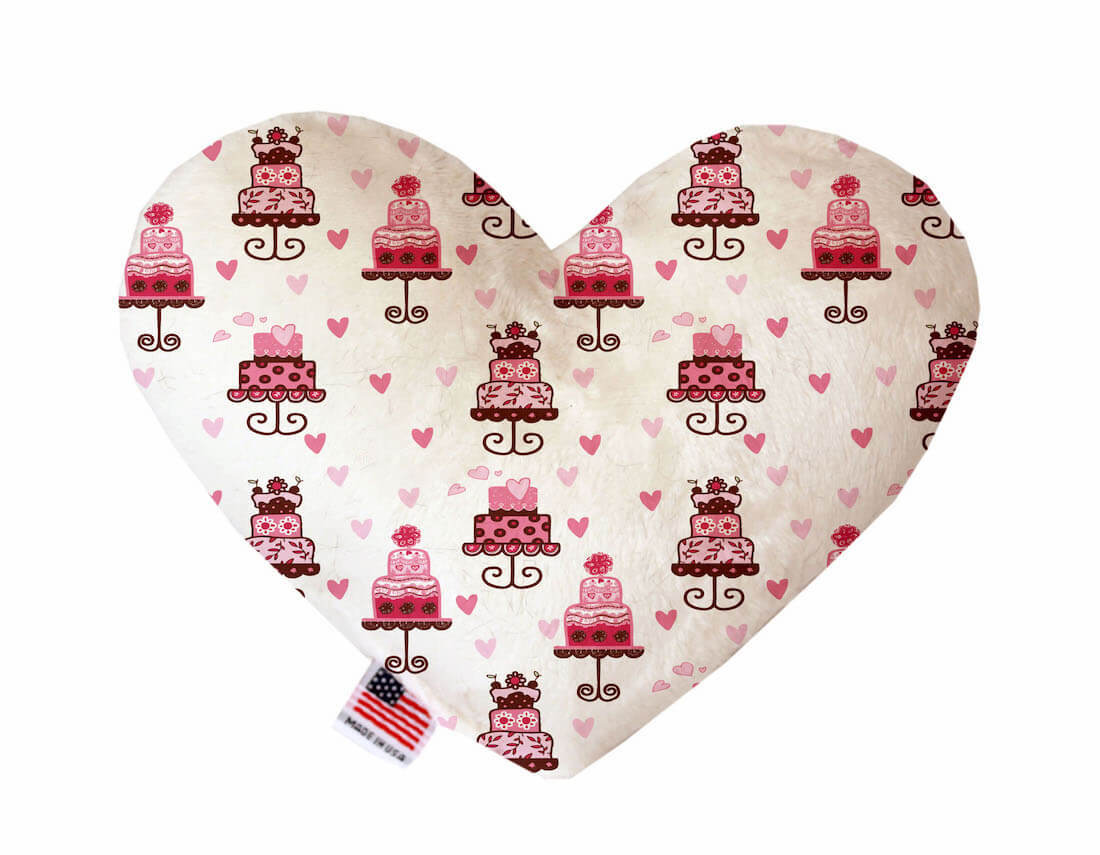 Heart shaped squeaker dog toy. White background printed with fancy pink cakes and hearts. Made in USA label on bottom trim.