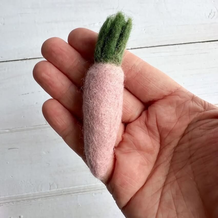 Someone holding a pink carrot felted wool cat toy in their hand to show size and scale.