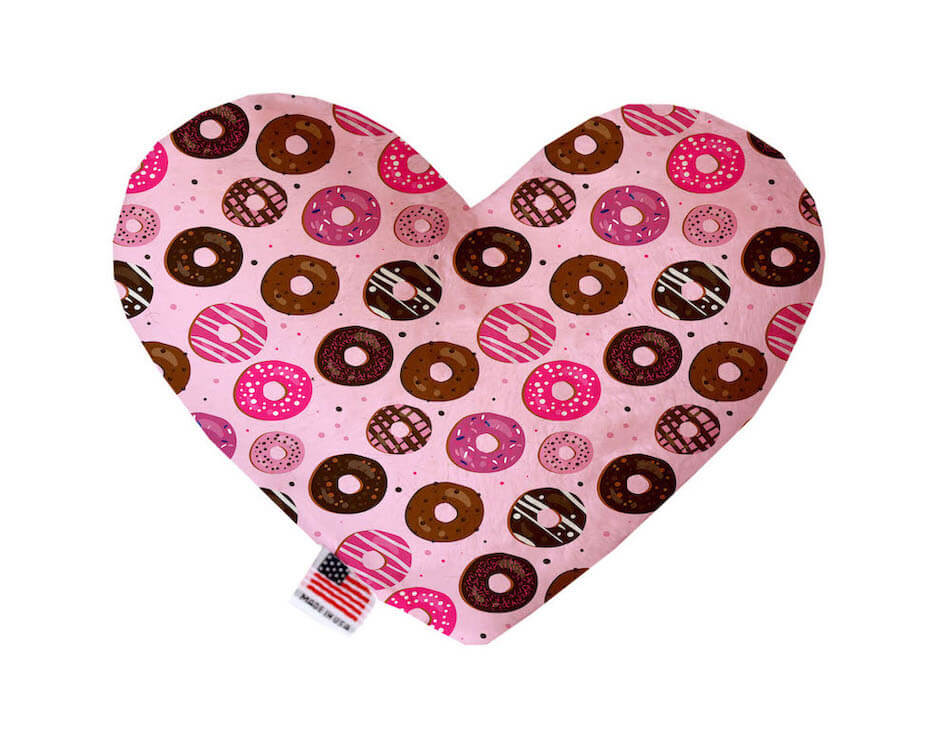 Heart shaped squeaker dog toy. Pink background with multicolored donuts. Made in USA label on bottom trim.