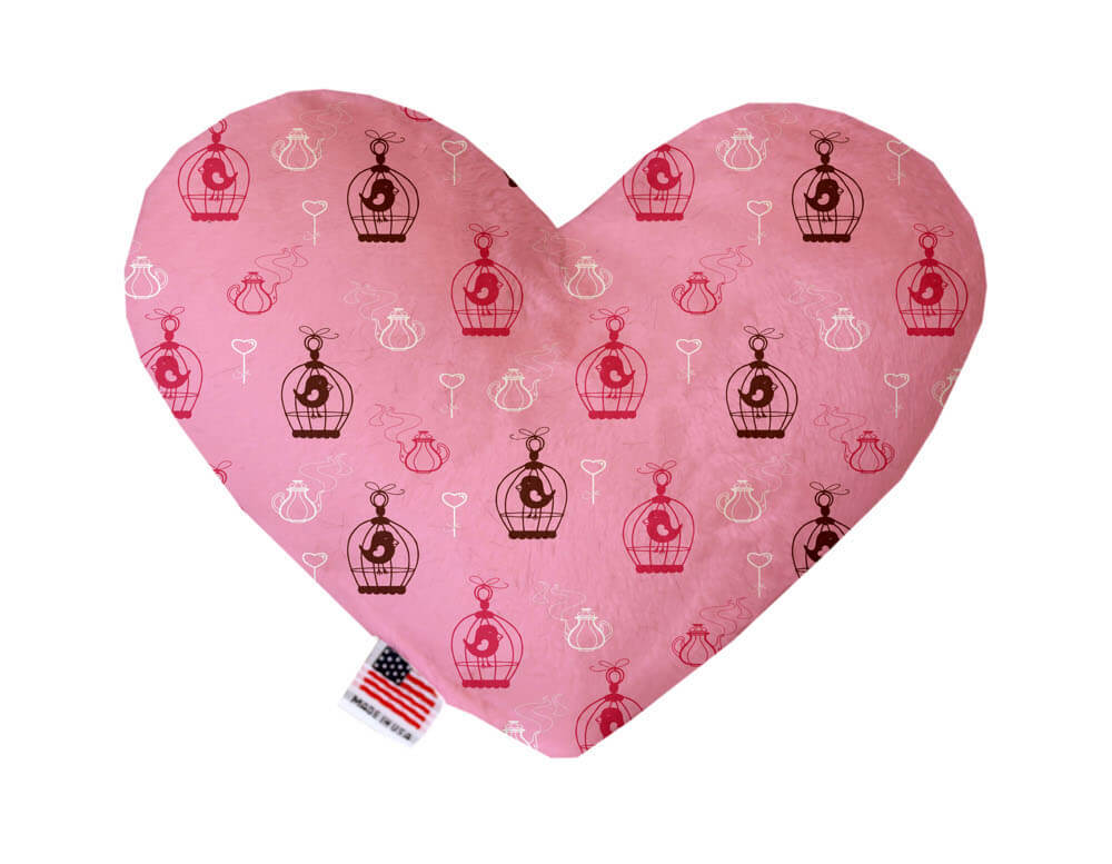 Heart shaped squeaker dog toy. Pink background with lovebirds in cages and heart shaped keys printed throughout. Made in USA label on bottom trim.