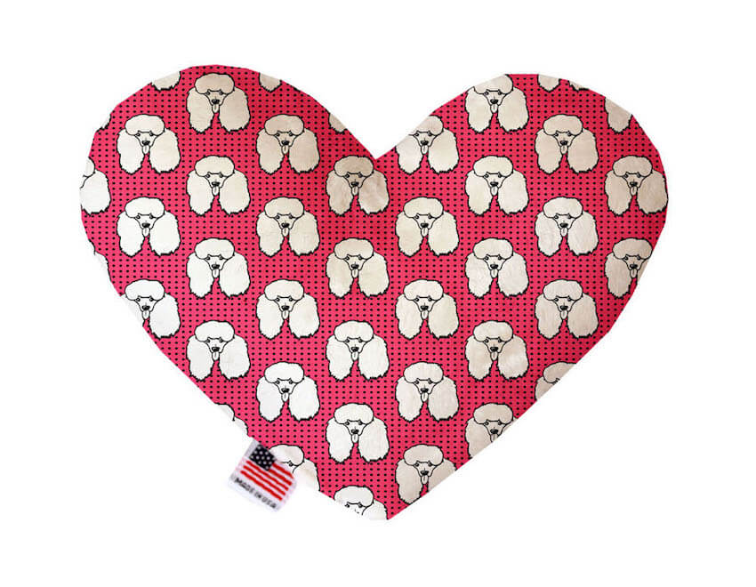 Heart shaped squeaker dog toy. Pink background with white poodle faces and tiny black polka dots printed throughout. Made in USA label on bottom trim.