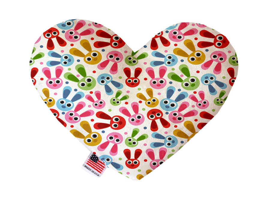 Heart shaped squeaker dog toy. White background with colorful bunny heads printed throughout. Made in USA label on bottom trim.
