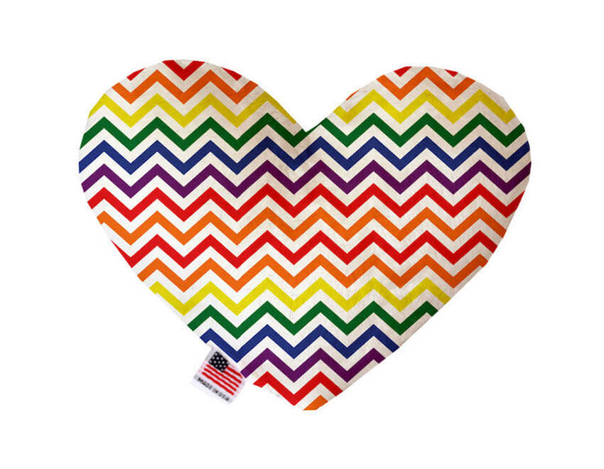 Heart shaped squeaker dog toy. White background with a rainbow chevron pattern printed throughout. Made in USA label on bottom trim.