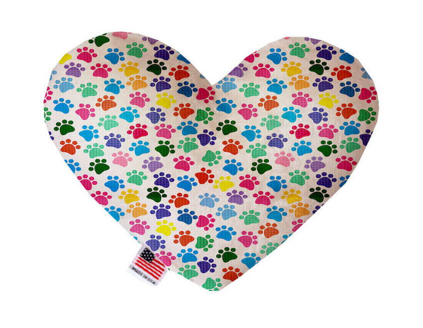 Heart shaped squeaker dog toy. White background with colorful paw prints printed throughout. Made in USA label on bottom trim.