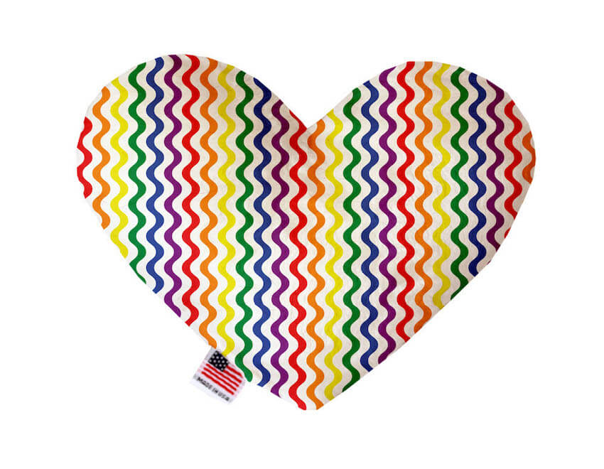 Heart shaped squeaker dog toy. White background with wavy rainbow stripes printed throughout. Made in USA label on bottom trim.