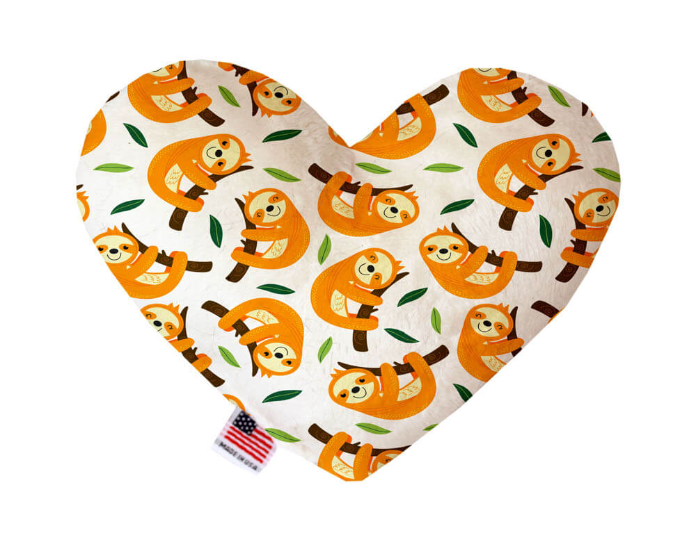 Heart shaped squeaker dog toy. White background with smiling sloths resting on tree branches printed throughout. Made in USA label on bottom trim.
