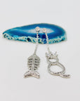 Cat and fishbone rhinestone drop earrings resting on blue agate stone.
