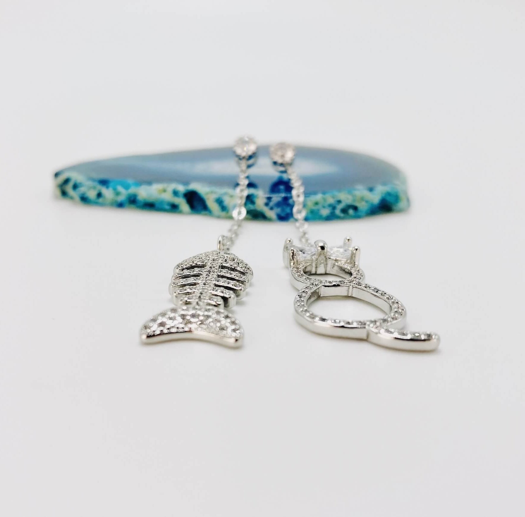 Cat and fishbone rhinestone drop earrings resting on blue agate stone.