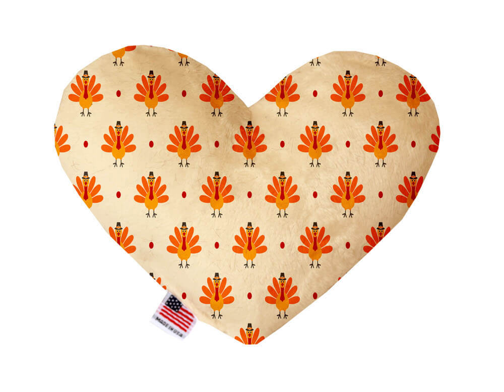 Heart shaped squeaker dog toy. Cream background with orange turkeys printed throughout. Made in USA label on bottom trim.