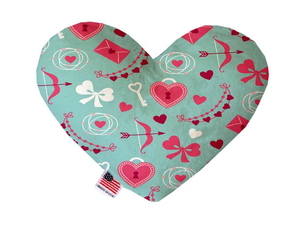 Heart shaped squeaker dog toy. Mint green background with red, pink and white hearts, bows, and Cupid's arrows of love printed throughout. Made in USA label on bottom trim.