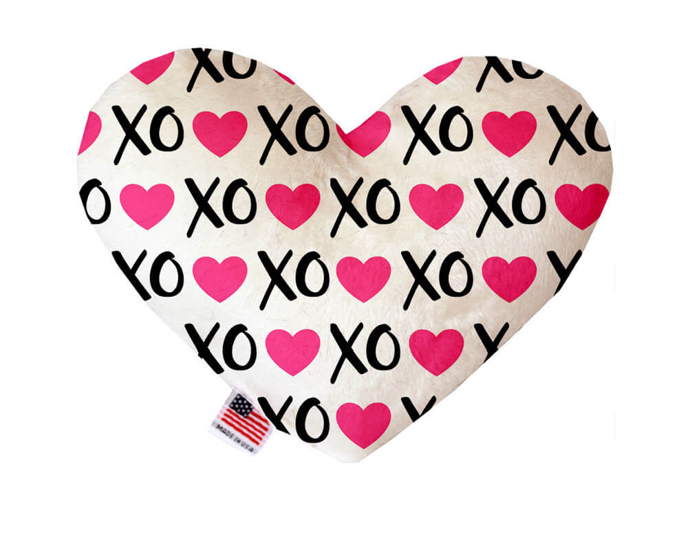 Heart shaped squeaker dog toy. White background with pink hearts and black "XO" text printed throughout. Made in USA label on bottom trim.