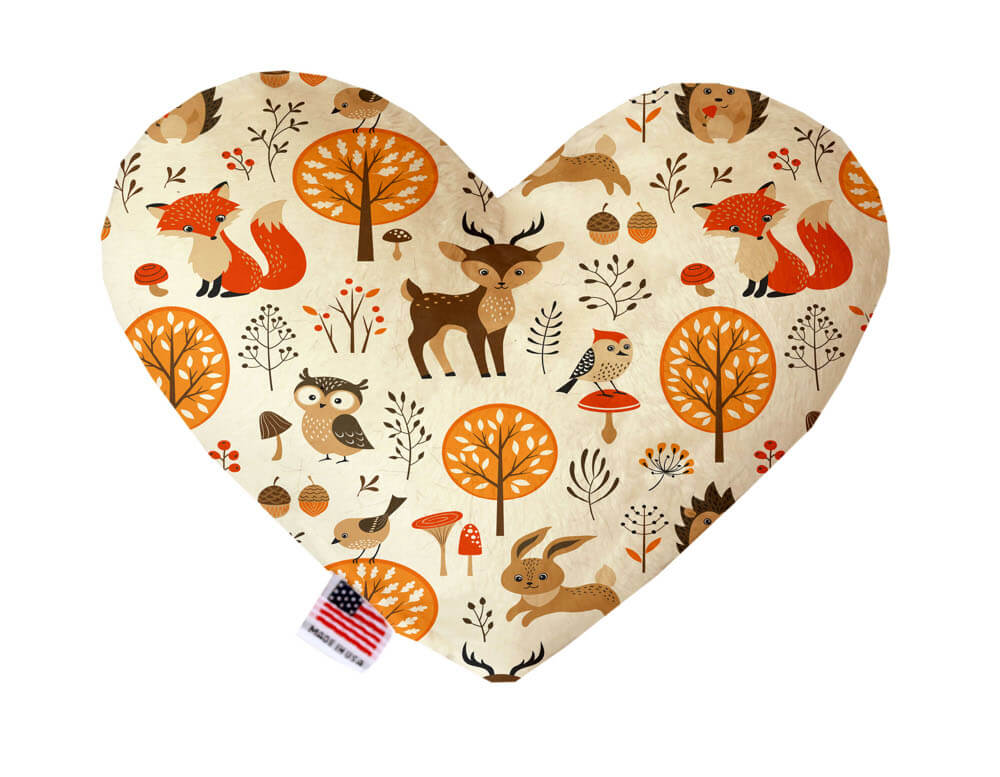 Heart shaped squeaker dog toy. Cream background with woodland animals such as foxes, deer, rabbits, owls and birds, as well as flora and fauna printed throughout. Made in USA label on bottom trim.